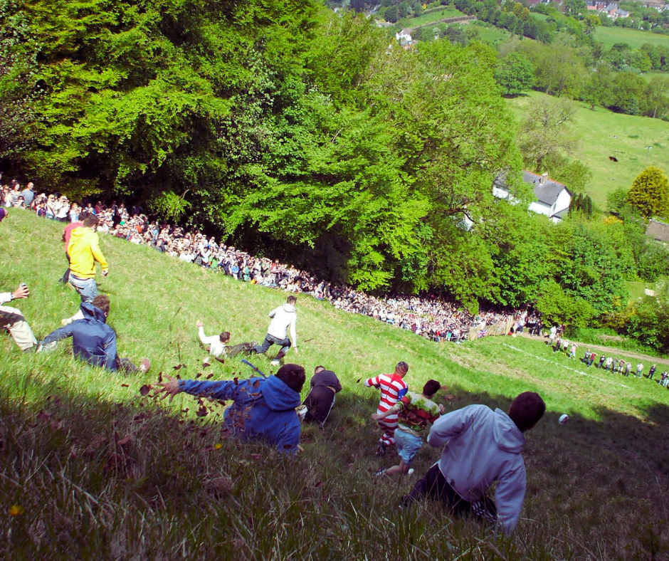 People scooting on their bottoms down the very steep Coopers Hill after a large wheel of double Gloucester cheese, during the cheese rolling festival.